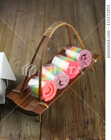 Rolls of colorful sponge cake on a wooden plate Rolls of colorful sponge cake on a wooden plate 115272855
