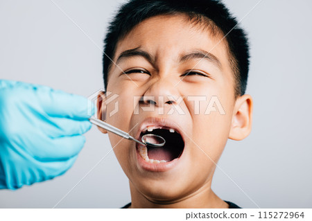 After removing a child's loose milk tooth a pediatric dentist conducts an examination. Dental tools assist in thorough check-up at dental office. Doctor uses mouth mirror to checking teeth cavity 115272964