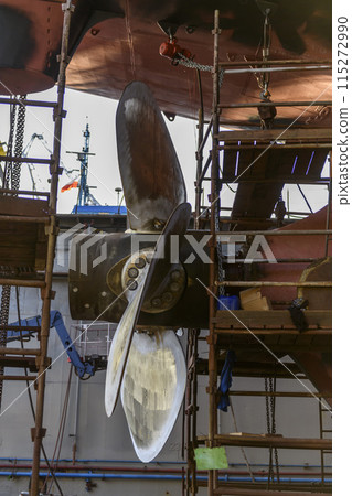 Cargo vessel in dry dock on ship repairing yard. Variable pitch propeller and rudder. Welder working on ship repairing yard. 115272990