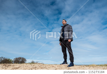 Low angle portrait of a 40 year old tall man, standing in the dunes, Knokke, Belgium Low angle portrait of a 40 year old tall man, standing in the dunes, Knokke, Belgium 115273184
