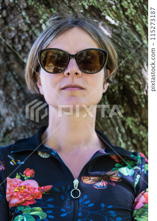 Picture of a relaxed attractive woman in the shadows of a tree against a trunk, Germany 115273187