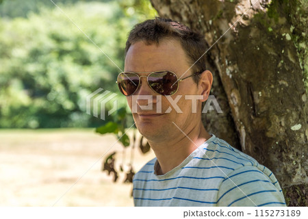 Head shot of a 40 yo man, standing relaxed against a tree in summer, Kordel,  Germany 115273189