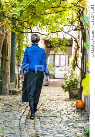 Attractive thirty year old white woman in a long dress walking down a narrow street with cobble stones Attractive thirty year old white woman in a long dress walking down a narrow street with cobble stones 115273191