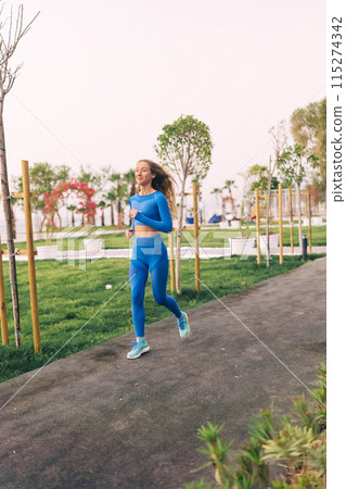Female Runner Jogging during Outdoor Workout in a Park. Female Runner Jogging during Outdoor Workout in a Park. 115274342