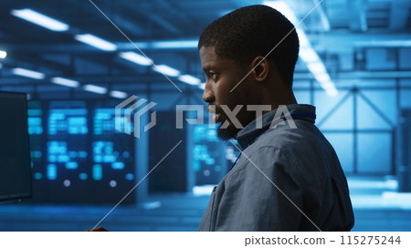 African american man working in server hub capable of processing vast amounts of data. IT programmer at PC desk typing on keyboard, updating servers controlling network resources, close up shot 115275244