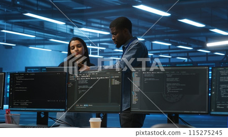 Multiethnic team of engineers uses laptop to do programming for servers providing computing resources for different workloads. Diverse colleagues using notebook to supervise data center supercomputers 115275245
