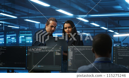 Multiethnic engineering team in server hub monitoring data center energy consumption across hardware using laptop. Multiracial colleagues inspecting supercomputers, ensuring malfunctions are fixed 115275246