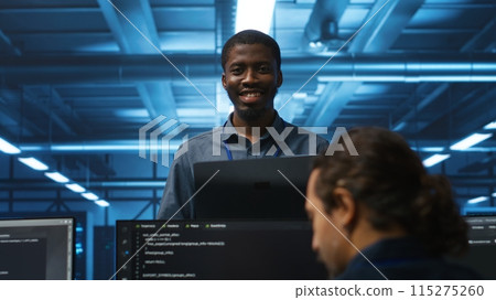 Portrait of cheerful african american manager supervising team in server room providing computing resources for workloads. Jolly supervisor oversees technicians in data center mending supercomputers 115275260