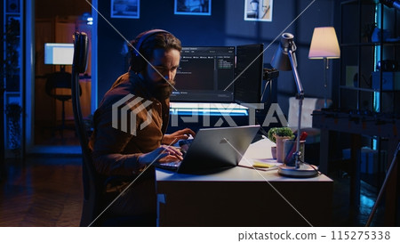 Developer typing code in home office, using Java programming language to develop software application. It professional using multimonitor PC setup and laptop to finish tasks, camera B 115275338
