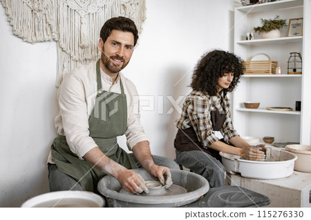 Man and woman shaping clay on pottery wheels in studio Man and woman shaping clay on pottery wheels in studio 115276330