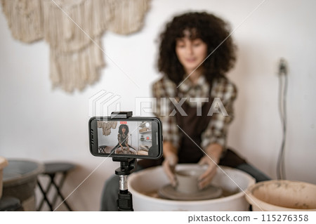 Young female potter recording video blog while sculpting pottery Young female potter recording video blog while sculpting pottery 115276358