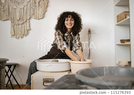 Female potter crafting ceramic pottery on wheel with a smile Female potter crafting ceramic pottery on wheel with a smile 115276393