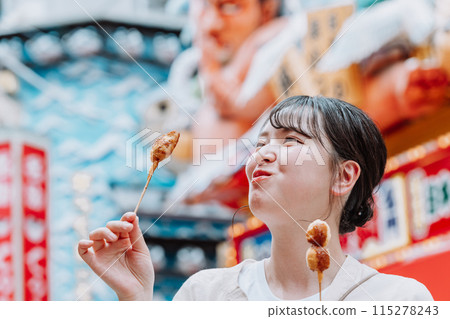 A young woman eating the famous kushikatsu in Shinsekai, Osaka 115278243