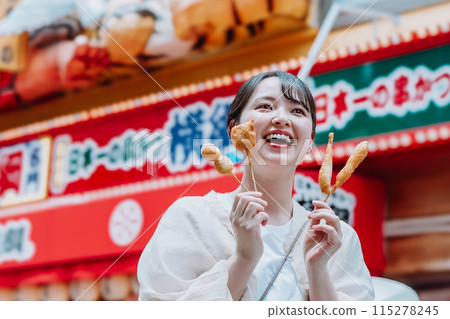 A young woman eating the famous kushikatsu in Shinsekai, Osaka 115278245
