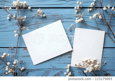 Card mockup, white blank wedding invitation with floral decor on bue wooden background. Greeting card mockup with white dried flowers on table 115279063