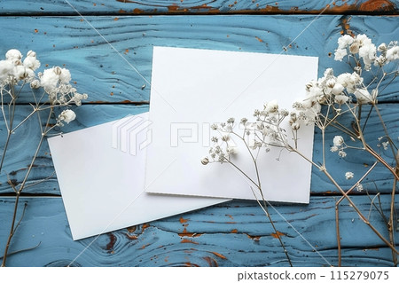 Card mockup, white blank wedding invitation with floral decor on bue wooden background. Greeting card mockup with white dried flowers on table 115279075