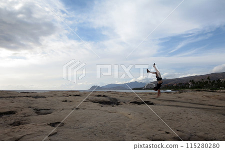 Man wearing a t-shirt, shorts, and slippers Handstands on shore rocks of Ko Olina Man wearing a t-shirt, shorts, and slippers Handstands on shore rocks of Ko Olina 115280280