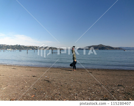 Man wearing a hoodie, pants, and shoes Handstands at on beach in Sausalito 115280407