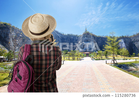 Female tourist enjoy taking photo of beautiful big stone buddha on the hill. Female tourist enjoy taking photo of beautiful big stone buddha on the hill. 115280736
