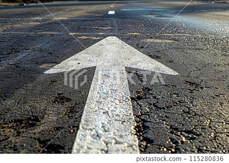 在筆直的柏油路上繪製的白色箭頭。 115280836
