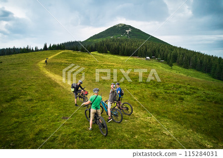 Group of cyclists men riding electric bikes outdoors. Happy tourists resting on the top of hill, enjoying beautiful mountain landscape. Concept of sport, active leisure and nature. Group of cyclists men riding electric bikes outdoors. Happy tourists resting on the top of hill, enjoying beautiful mountain landscape. Concept of sport, active leisure and nature. 115284031