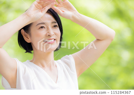 A middle-aged woman blocking the sunlight with her hand amidst fresh greenery 115284367