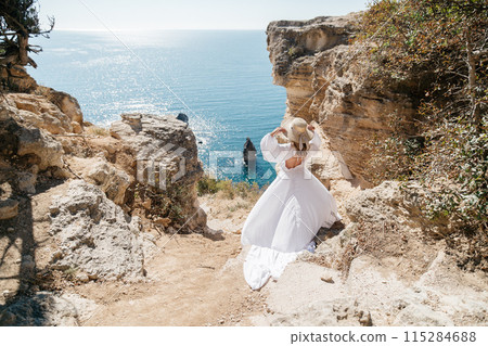 A woman in a white dress is walking on a rocky beach near the ocean. The scene is serene and peaceful, with the woman's dress flowing in the wind. A woman in a white dress is walking on a rocky beach near the ocean. The scene is serene and peaceful, with the woman's dress flowing in the wind. 115284688