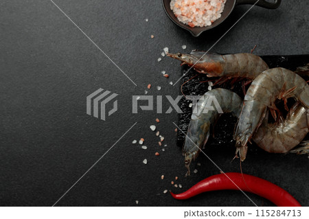 Large king prawns raw on a black cutting board. Hot pepper, salt. Black background Large king prawns raw on a black cutting board. Hot pepper, salt. Black background 115284713