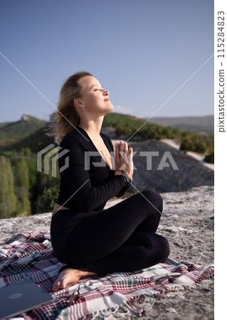A woman is sitting on a blanket with her hands on her knees 115284823
