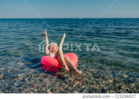 A woman is floating on a pink inflatable raft in the ocean A woman is floating on a pink inflatable raft in the ocean 115284827