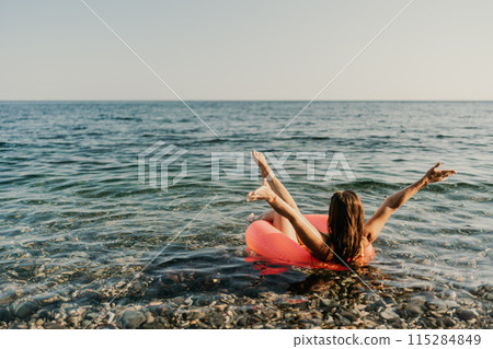A woman is floating in a red inflatable tube in the ocean 115284849