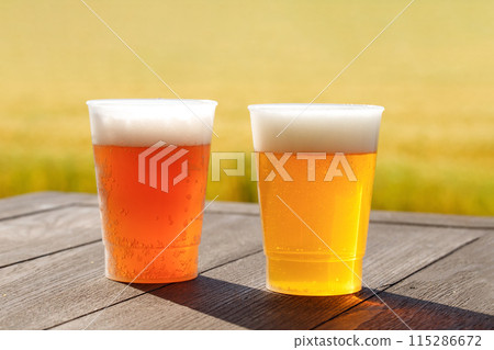 Two types of beer are placed on the table. They are served in plastic cups. Wheat field background. 115286672
