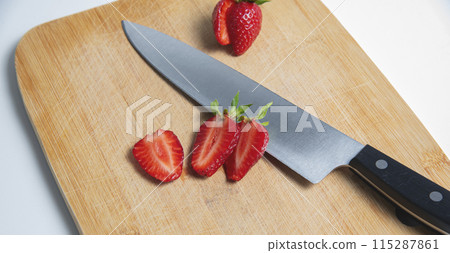 The strawberries are cut into slices. they lie on a wooden board and next to the knife The strawberries are cut into slices. they lie on a wooden board and next to the knife 115287861