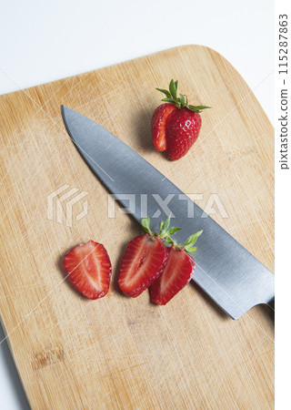 The strawberries are cut into slices. they lie on a wooden board and next to the knife The strawberries are cut into slices. they lie on a wooden board and next to the knife 115287863