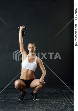 Kettle bell, woman and overhead exercise in gym, squat and strength on dark background. Sport, weight lifting and bodybuilder for female person, muscular or sportswear for athlete and health training 115288285