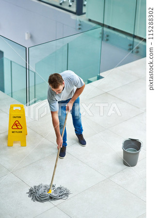 Man, janitor and mopping office floor or cleaning hygiene with caution sign or water, soap or bacteria. Male person, disinfection and corporate building as washing service or dirty, wellness or job Man, janitor and mopping office floor or cleaning hygiene with caution sign or water, soap or bacteria. Male person, disinfection and corporate building as washing service or dirty, wellness or job 115288302