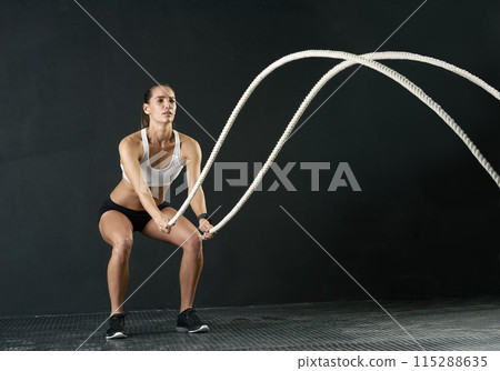 Woman, studio and training with battle rope for fitness, calorie and body workout for vitality or wellness. Girl, squat and exercise on black background for strength, power and endurance or gym 115288635