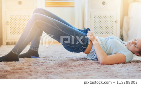 Woman, home and struggle with jeans on floor for dressing, weight gain, force and tight. Lens flare, female person and bedroom with lying on floor to squeeze small pants for outfit, fashion and style 115289802