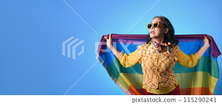Elegant senior lady holding rainbow flag on blue background. LGBT, human rights, freedom and equality concept 115290241