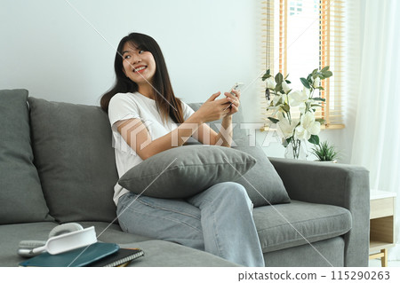 Relaxed young Asian woman using mobile phone on a couch at home 115290263