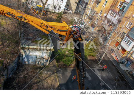 Municipal service workers stand with a chainsaw in a crane basket and trim dangerous trees Municipal service workers stand with a chainsaw in a crane basket and trim dangerous trees 115293095