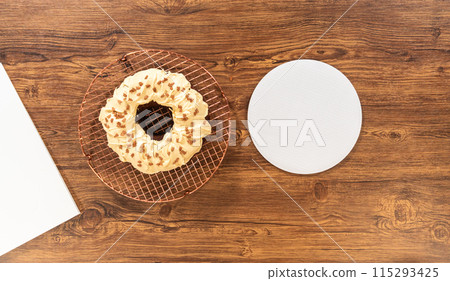 Flat lay. Carefully placing the gingerbread bundt cake, adorned with salted caramel frosting and gingerbread sprinkles, into a white paper bundt cake box with a clear window for gifting. 115293425