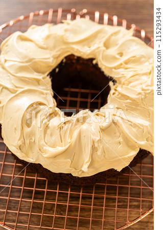A gingerbread bundt cake being generously frosted with salted caramel frosting and topped with delightful gingerbread sprinkles. 115293434