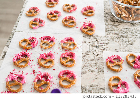 Freshly dipped and still glistening, these crunchy pretzels are lovingly adorned with pink chocolate and a scattering of colorful sprinkles, promising a feast for the senses. 115293435