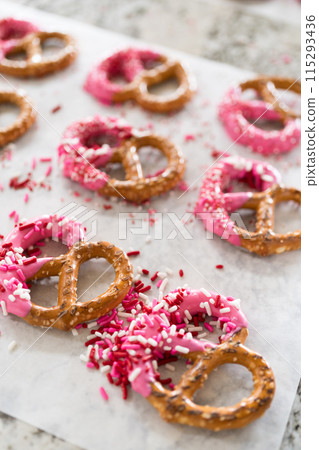 Freshly dipped and still glistening, these crunchy pretzels are lovingly adorned with pink chocolate and a scattering of colorful sprinkles, promising a feast for the senses. 115293436