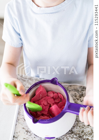Eager eyes focus on the pot of vibrant, melting candy as a young cook gently swirls the mixture, poised to transform plain snacks into delectable treats. Eager eyes focus on the pot of vibrant, melting candy as a young cook gently swirls the mixture, poised to transform plain snacks into delectable treats. 115293441