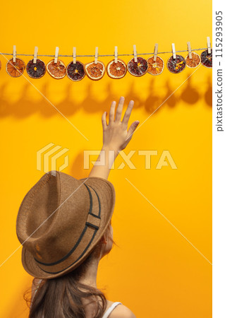 Girl reaches for dried orange slices hanging on a rope. Girl reaches for dried orange slices hanging on a rope. 115293905