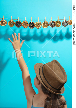 Girl reaches for dried orange slices hanging on a rope. Girl reaches for dried orange slices hanging on a rope. 115293906