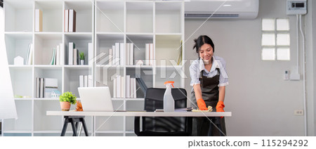 Female office cleaner smiling while wiping desk. Concept of workplace cleanliness 115294292