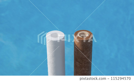 Two water filter cartridges, one clean and one dirty, next to a swimming pool. 115294570